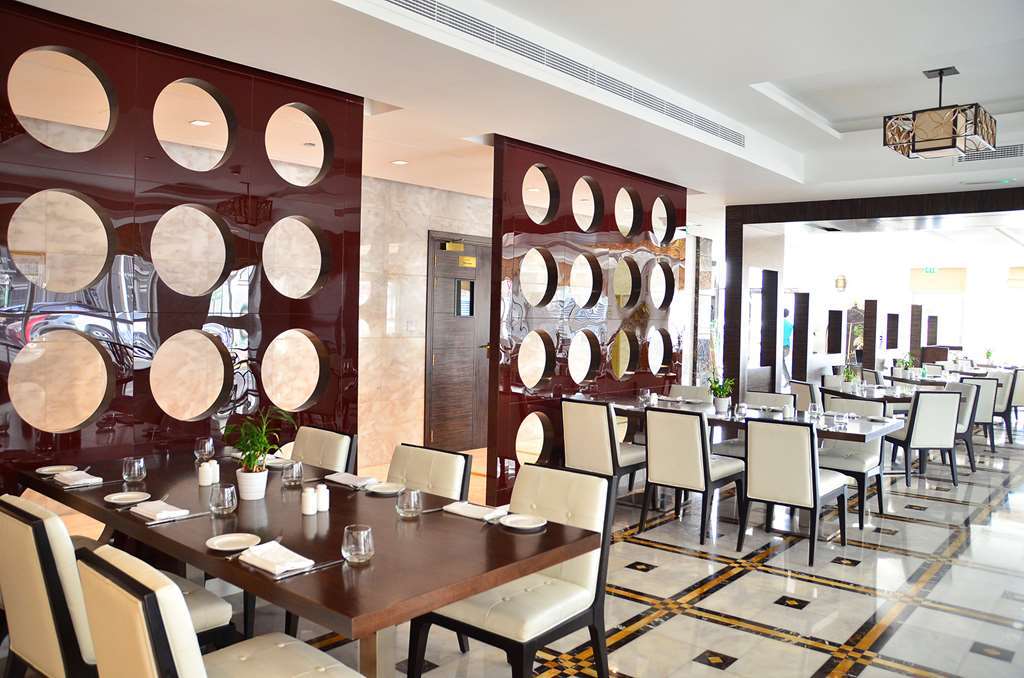 占奈萨拉卜塔酒店 阿布扎比 外观 照片 The photo shows a modern restaurant interior. It features a series of tables with elegant place settings and comfortable chairs. The walls are decorated with a unique design, displaying round mirrors or circular elements set in a polished brown panel