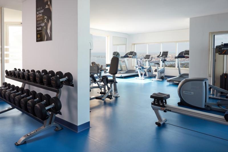 占奈萨拉卜塔酒店 阿布扎比 外观 照片 The photo shows a modern gym or fitness area. On one side, there is a rack of dumbbells arranged in order of weight. In the background, several pieces of gym equipment are visible, including treadmills and stationary bikes. The space features large w
